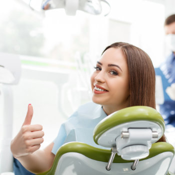 satisfied young brunette sitting in the dental chair and showing her thumb up